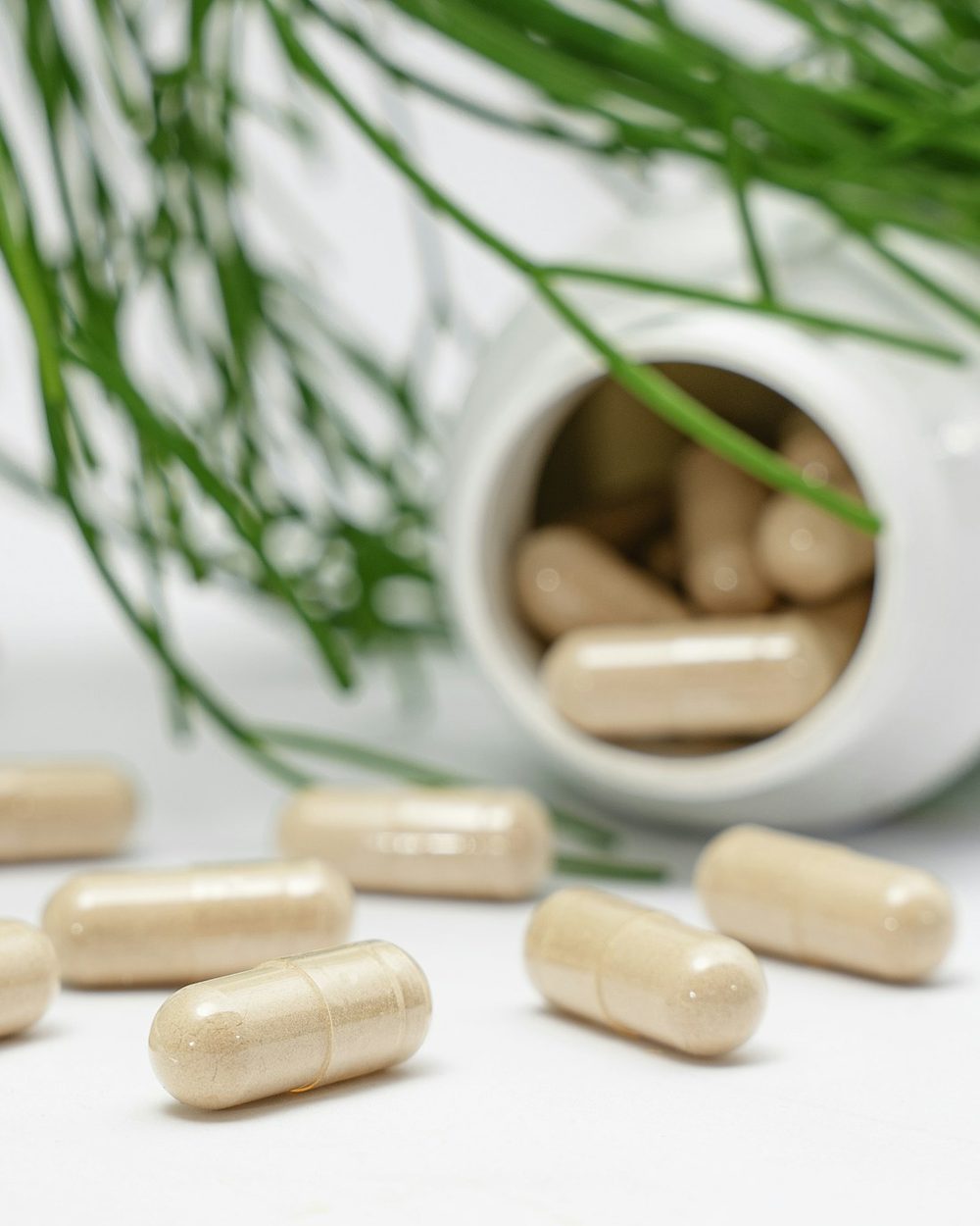 Natural supplement capsules spilling from a jar beside fresh greens — individualized functional-medicine care
